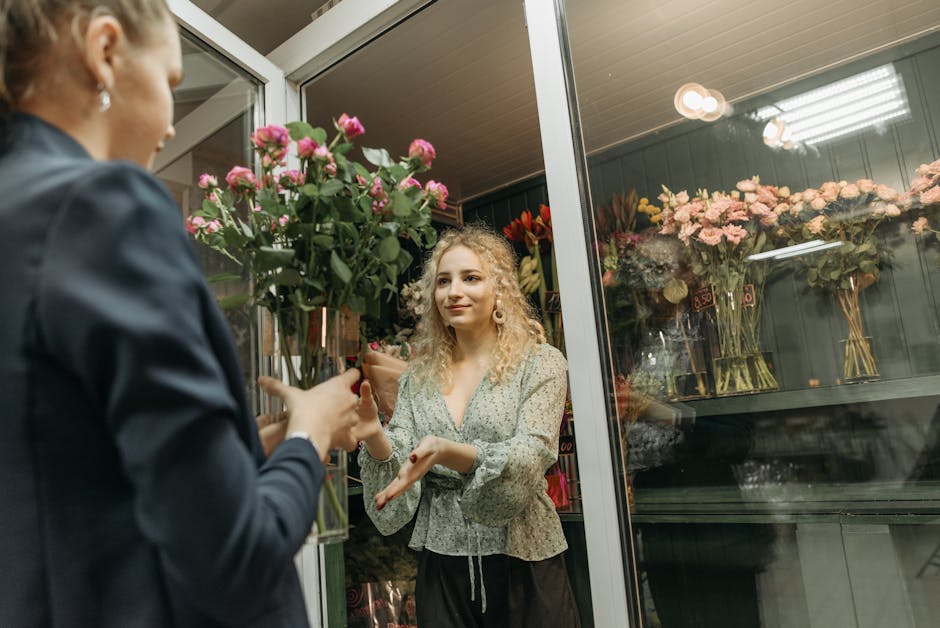 A florist from Osidge flower delivery service hands a bouquet of fresh pink roses to a female customer inside a floral shop. The bouquet is wrapped in brown paper with green stems and vibrant pink pet