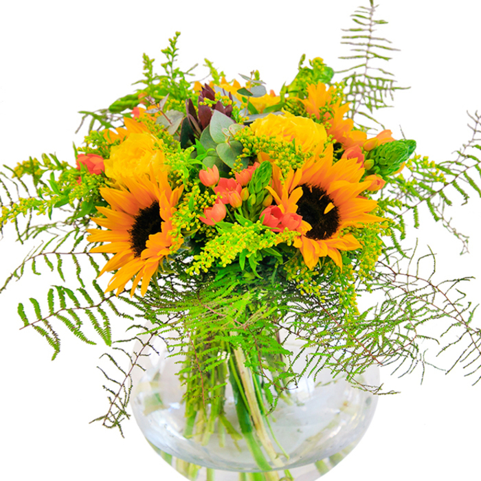 Overflowing with seasonal splendour, this bouquet is expertly arranged to mirror the sunny spirit of Osidge. At its heart are radiant sunflowers-petals wide and golden, encircling deep brown centers that draw the eye much like summer's brightest days in Oak Hill Park. Interwoven with these sunbeams are classic yellow roses, their tightly coiled petals and muted gold tones imparting a sense of refinement and softness. Scarlet Hypericum berries, shiny and round, cluster amidst the greenery-providing captivating pops of colour that uplift the dominant yellows. Wisps of green fern, lacy and feather-light, spill gracefully around the edges, while filler stems-possibly local solidago-contribute threads of delicate yellow. Bluish green eucalyptus leaves and slim, spear-like spikes add subtle layers and aromatic freshness, enhancing the natural richness of the setting. Set within a crystal-clear, spherical glass vase, the entwined stems dip into cool water, the arrangement as a whole glowing in natural light. The bouquet's collective fragrance-a gentle duet of rose and greenery-is just enough to enliven any room. Perfect for anniversaries, congratulations, or simply bringing a sunlit touch to a neighbour's home along Osidge Lane, this arrangement is a testament to the expertise and heartfelt care of Osidge florists. Every flower and leaf is chosen to reflect the joyful rhythms of local life.