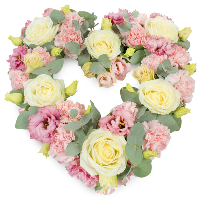 A full, heart-shaped floral tribute is arranged in a harmonious blend of pastel tones, displayed against a pure white background that lets every nuance of colour and shape stand out. Cream and soft butter-yellow roses are spaced around the heart, their velvety petals layered in tight spirals that gradually unfurl toward the outer edges, giving the impression of quiet strength and devotion. Between these roses, ruffled light pink carnations fill the gaps, forming dense cushions of petal upon petal that soften the overall silhouette and add a sense of cosy abundance. Deeper pink to mauve lisianthus blooms are interspersed with care, their more open, fluted petals carrying a slightly richer tone that draws the eye gently through the arrangement. Silvery eucalyptus foliage weaves in and out, its rounded leaves arching along the curves of the heart and providing a cool, calming green-grey backdrop, much like the soothing greenery you might see in the quieter streets and gardens around Osidge and New Southgate. Tiny yellow-green flower buds appear intermittently, suggesting freshness and renewal even within the setting of farewell. The flowers are packed closely, with no gaps in the outline, creating a luxurious heart shape that appears soft, comforting, and complete. This is the kind of sympathy wreath a family in Osidge might choose for a funeral service at a local crematorium or a memorial gathering at a community hall, where they wish to express love, remembrance, and respect with understated elegance. The overall feeling is one of gentle peace, dignified sorrow, and gratitude for a life well lived.